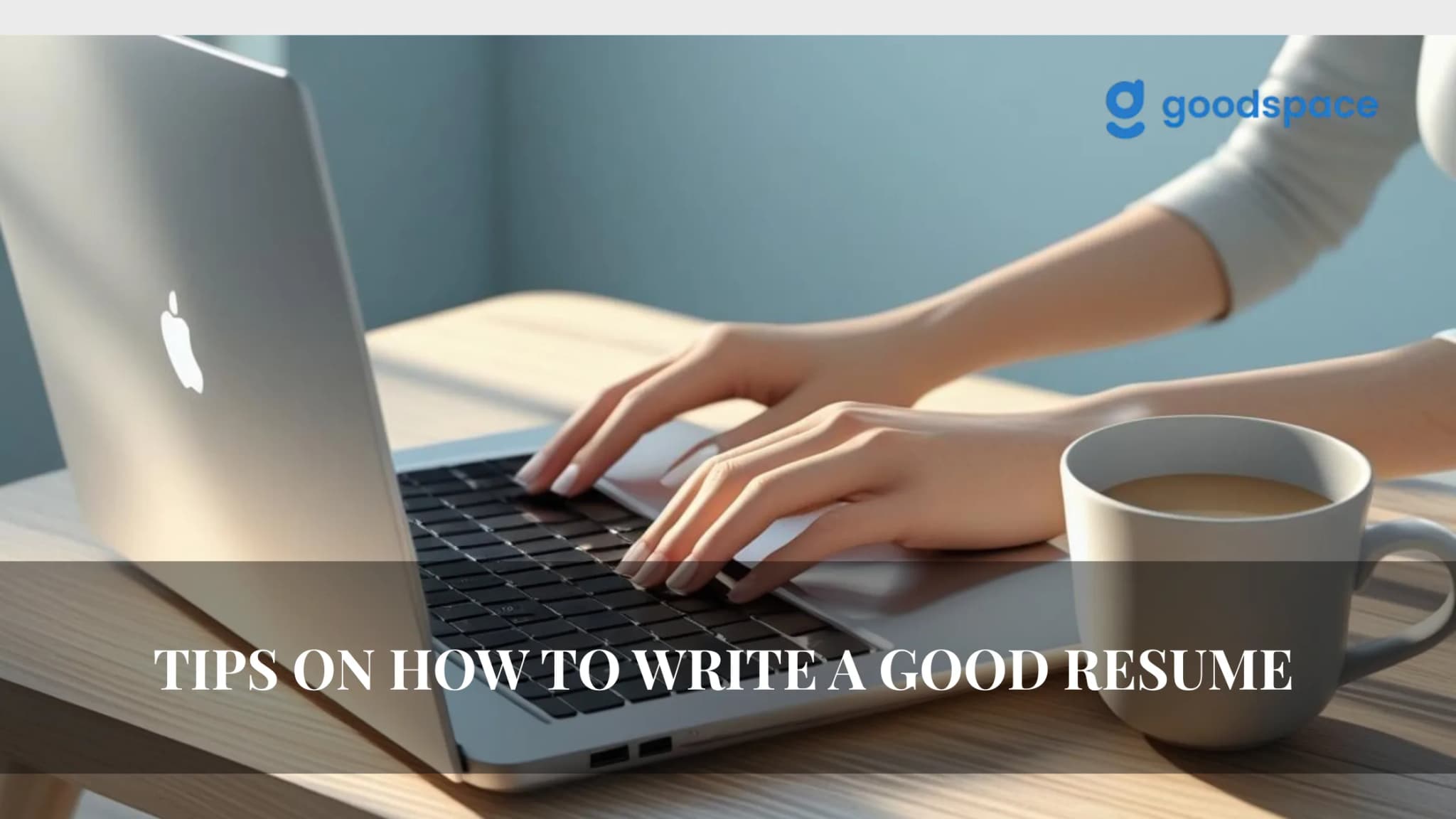 Photo of hands typing on a silver laptop at a wooden table with a mug of coffee